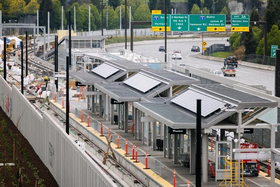 A photo looking down on the Judkins Park Station platform during construction with westbound freeway traffic in the background and a retaining wall in the foreground.