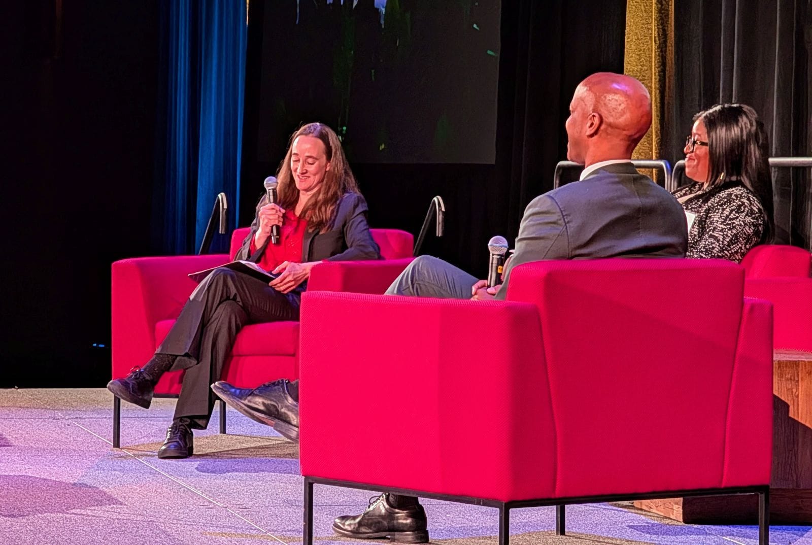 The three leaders sit in big red chairs and hold microphones.