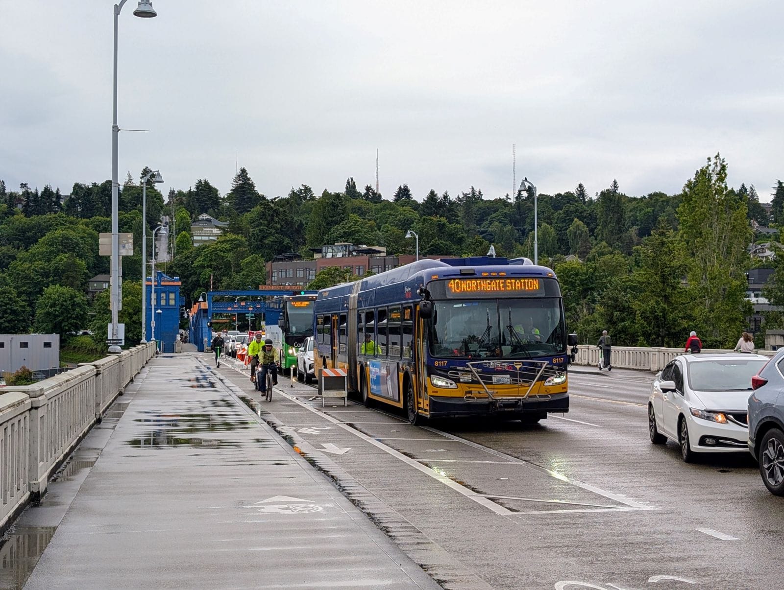 Route 40 waits in heavy car traffic on the north end of the bridge as two people biking pass in the bike lane.