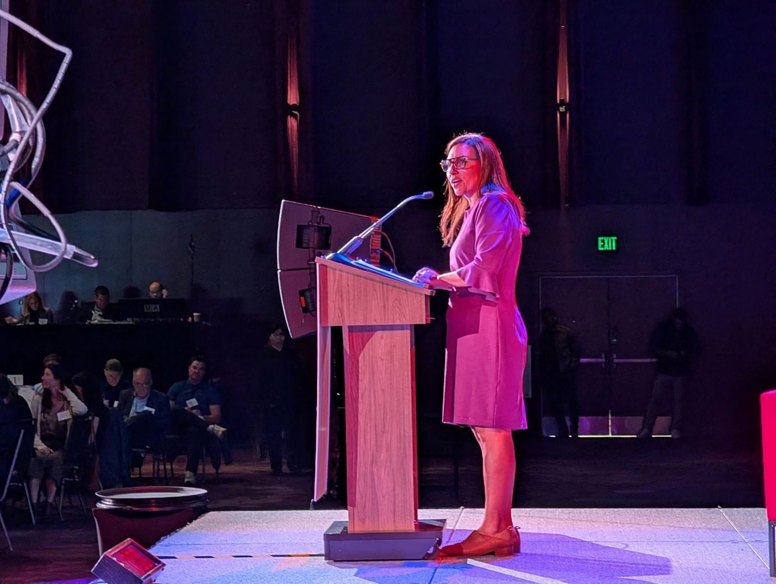 Mosqueda stands at a lectern with tables full of luncheon guests looking on.