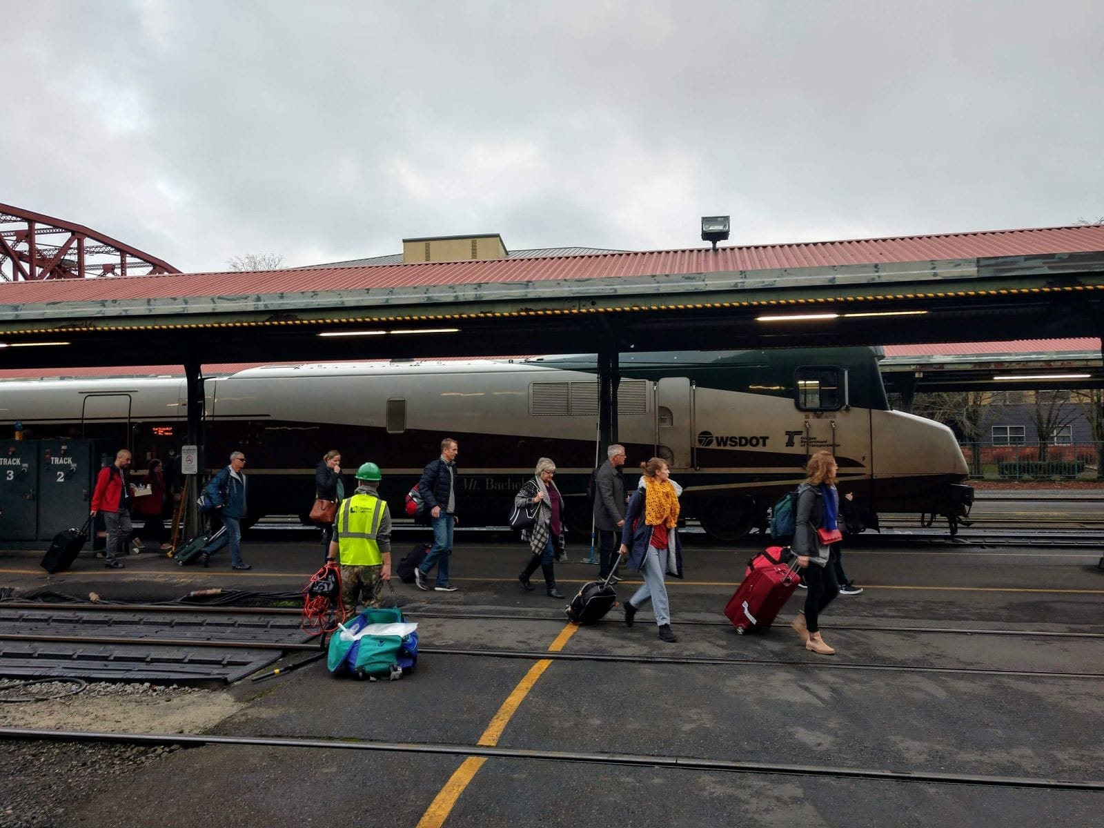 Passengers exit a Cascades train in Portland with luggage in town on a gray cloudy day.