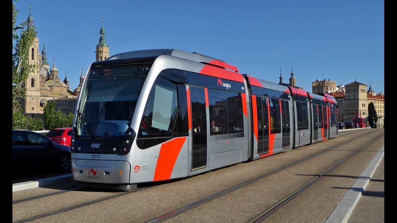A long streetcar on a quiet urban street in Spain with church spire in the background