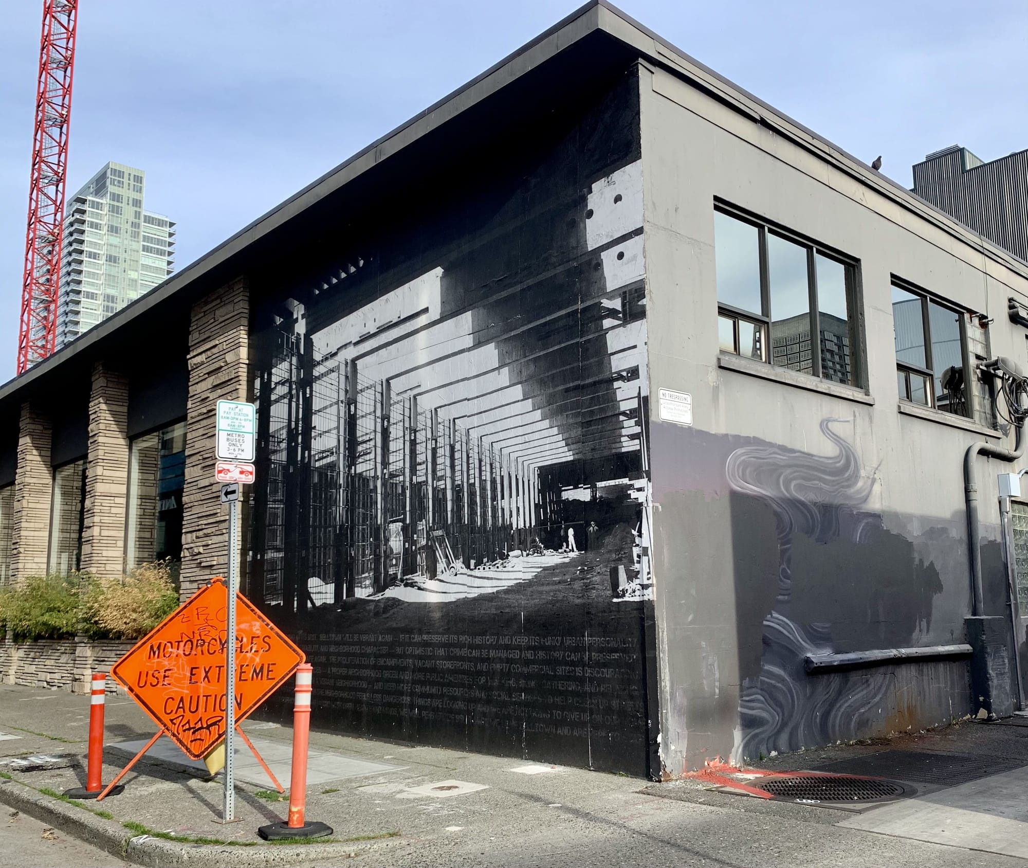 A photo of a black and white mural of a tunnel on the side of a one story building with a road construction sign in front of it.