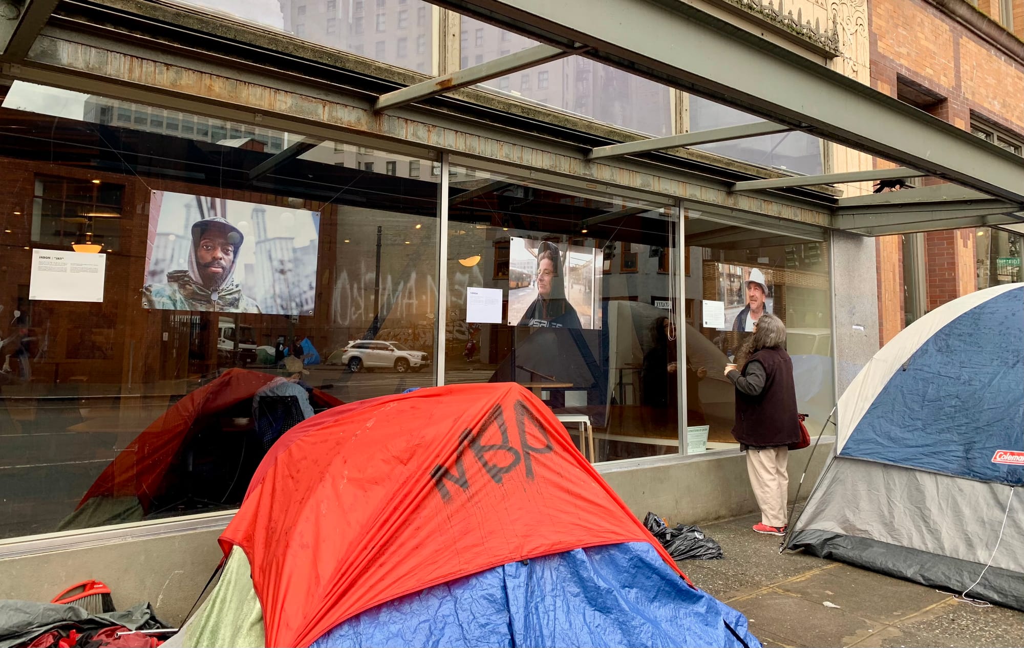 A photo of a tent in front of a glass window with exhibiting large portrait style photos of people.