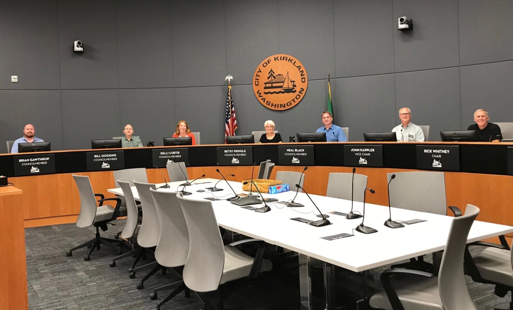 
                     A photo of people sitting in a city council chamber.
                     