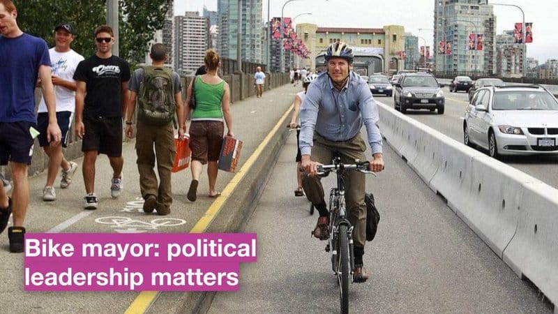 Image is road with a concrete barrier separating car traffic and protecting the bike lane and sidewalk. A caption reads: "Bike Mayor: Political leadership matters"
