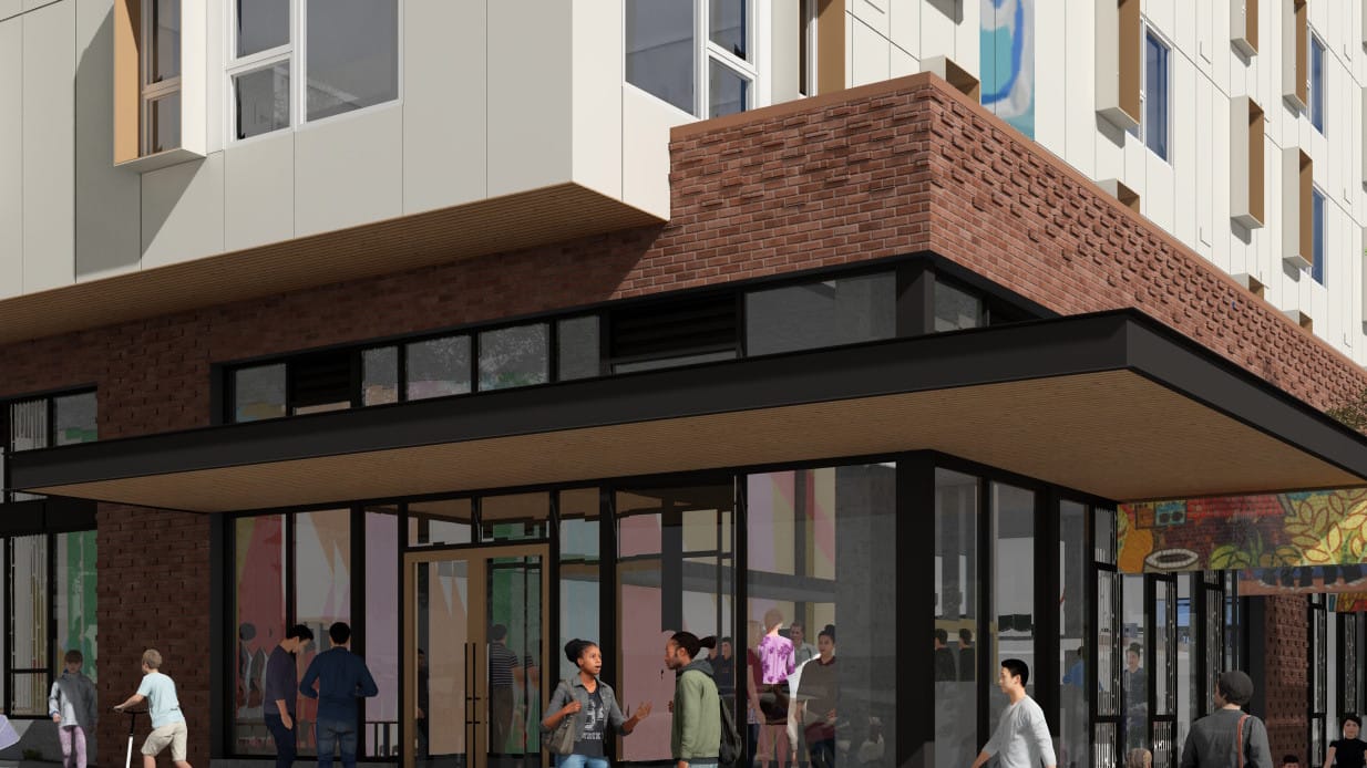 The image shows people gathered around the first floor retail which is clad in brick. Housing with white siding is above.