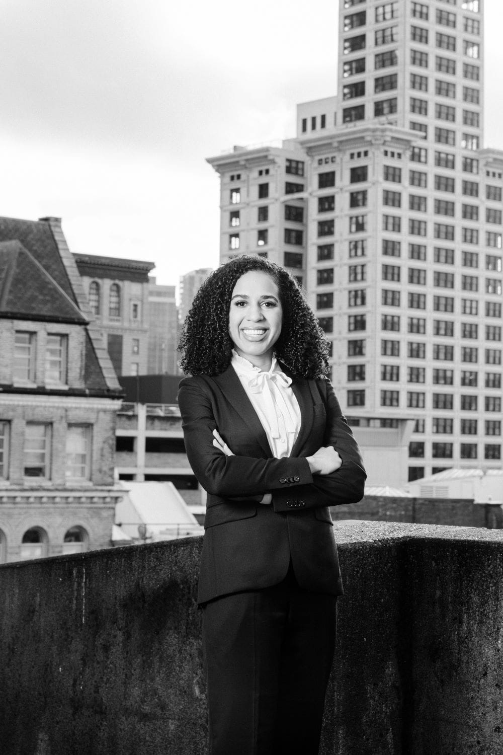 Evans crosses her arms and stands on a rooftop with the Smith Tower in the background.