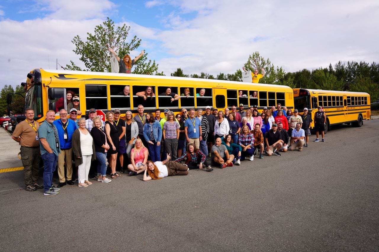 The school district's transportation team poses with a big yellow school bus.