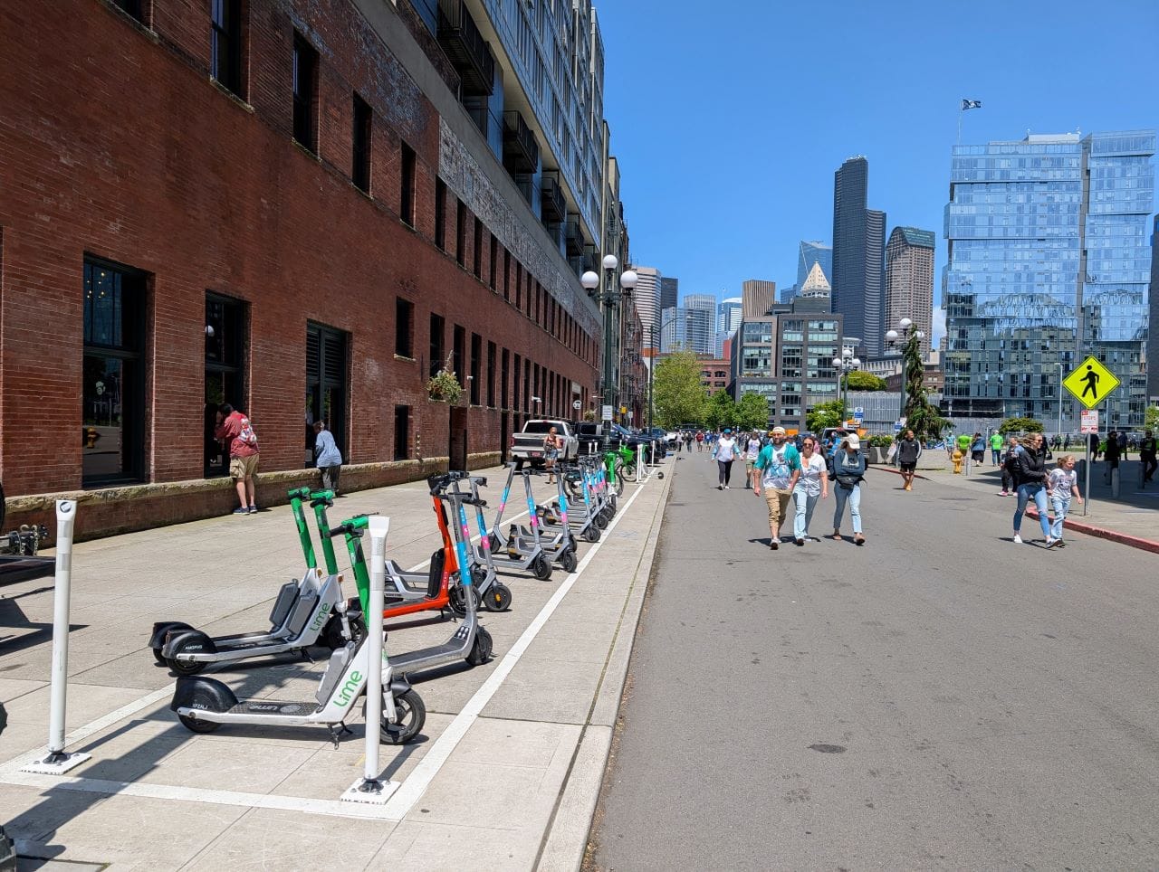 Mariners fans walk to a baseball game in the middle of Occidental with the parking corral on the sidewalk helping to keep the main pedestrian thoroughfare clear. 