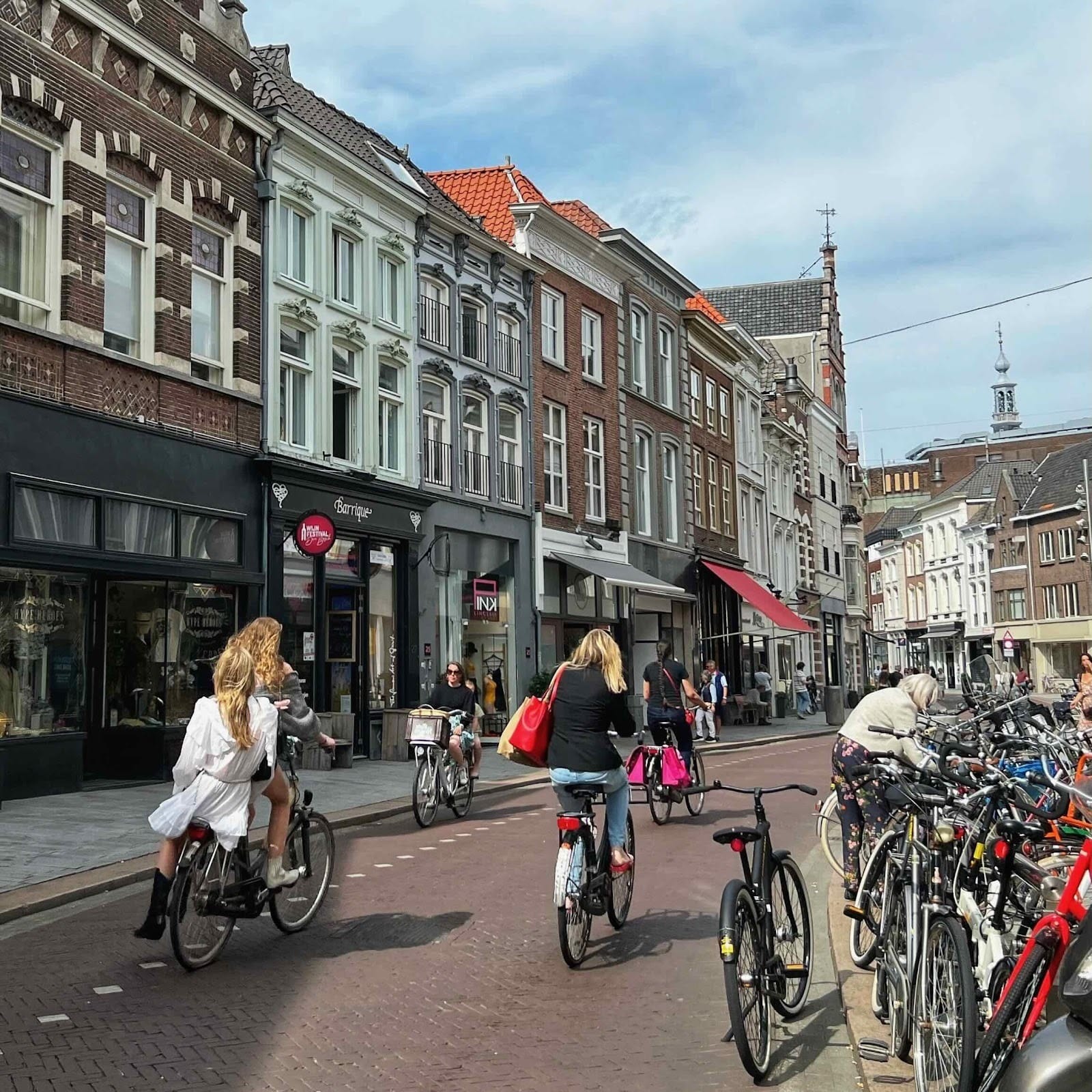 The streets is busy with people biking, including one woman giving her friend a ride on the back of her bike.