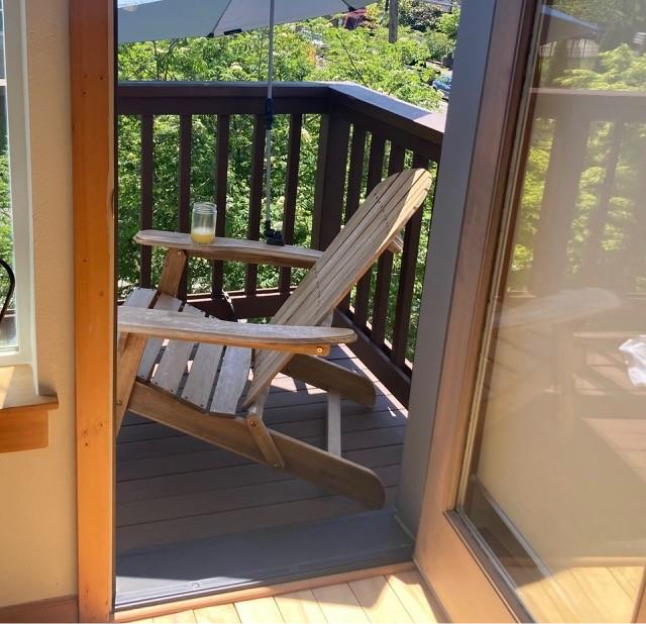An Adirondack chair on a small balcony with trees in the distance