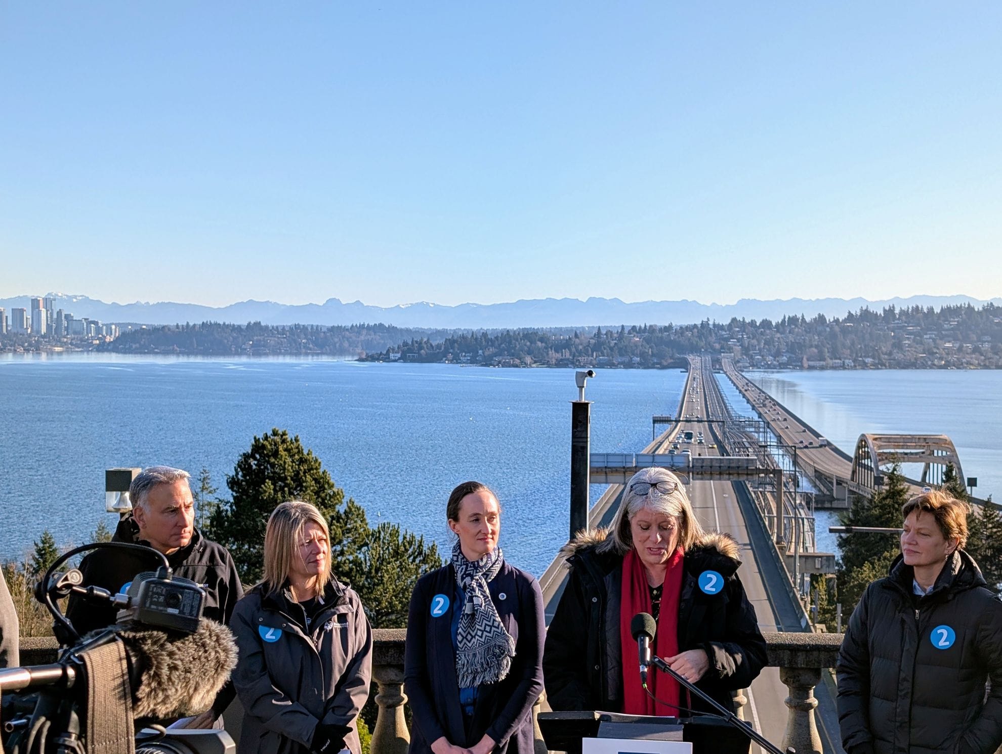 Lake Washington and the I-90 floating bridge is visible in the background behind CEO Dow Constantine, Redmond Mayor Angela Birney, Seattle Mayor Katie Wilson, and Claudia Balducci.