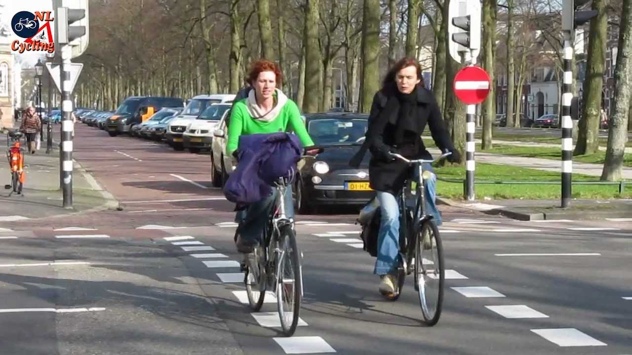 Two woman bike without helmets on a street with a bike lane.