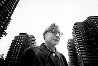Jane Jacobs in glasses with apartment towers in the background.