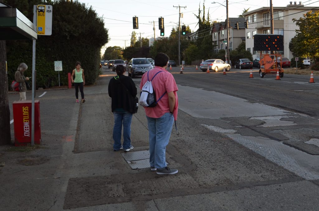 People wait for the bus on Greenwood Avenue N. and NW 117th St. To access this stop pedestrians run a gauntlet of parked cars, bushes in the public ROW and speeding cars. (photo by author)