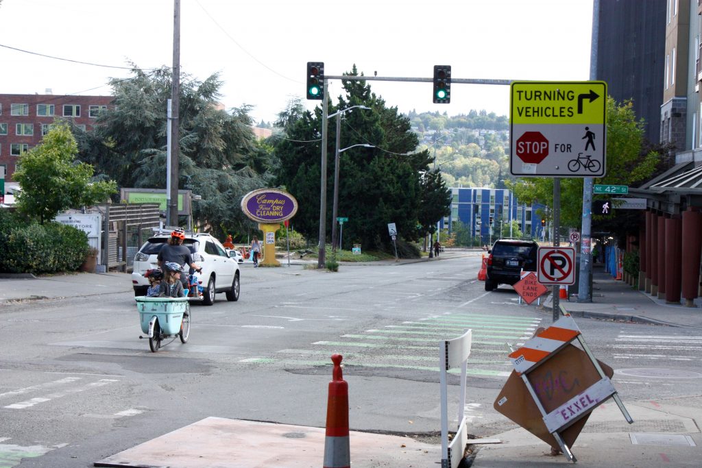 A mother braves into traffic with two kids in tow since the future protected bike lane is currently protected parking.