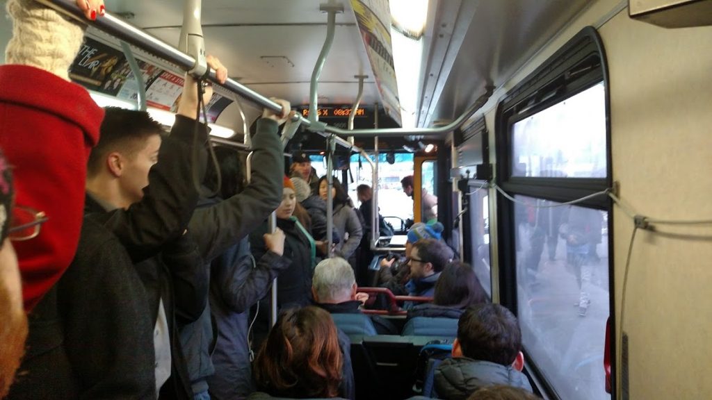 People hold on to the overhead handle on a standing room bus headed down Aurora.