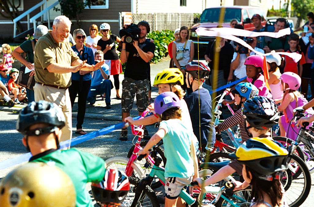 Mayor Mike McGinn cutting the ribbon on the Ballard Neighborhood Greenway as kids on bikes line up to get a first ride. (Credit: Dennis Bratland)