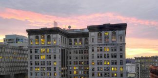 King County Grapples with Public Defender Crisis A ten story building with a pinkish purple sunset in the background