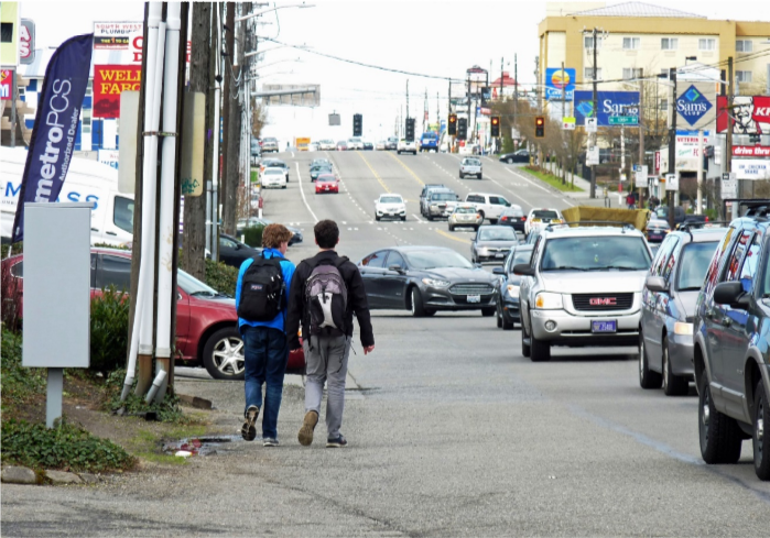Two teens walk along the edge of Aurora with no sidewalk and streams of cars going by.