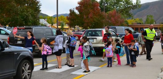 A school crosswalk busy with students and parents in a sea of cars.