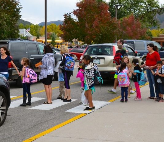 Car-Based School Commutes Hurt Families with Kids A school crosswalk busy with students and parents in a sea of cars.