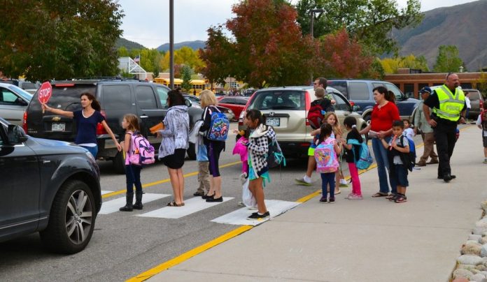A school crosswalk busy with students and parents in a sea of cars.