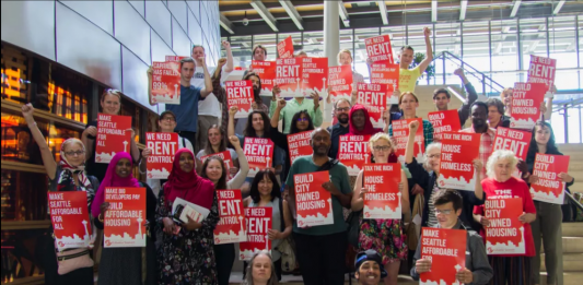 Advocates hold red signs backing rent control and housing the homeless.