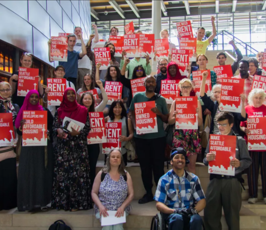 Tenant Advocates Win Seattle Eviction Ban Extension and Press for Broader Reforms Advocates hold red signs backing rent control and housing the homeless.