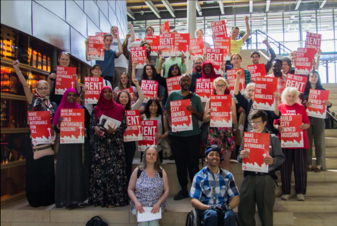 Advocates hold red signs backing rent control and housing the homeless.