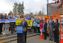 The Radical Promise of Vision Zero Mayor Ed Murray stands at a podium behind a crowd of staff and advocates with safety-themed signs. An electronic street signs also displays "Vison Zero."
