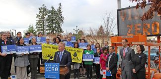 Mayor Ed Murray stands at a podium behind a crowd of staff and advocates with safety-themed signs. An electronic street signs also displays "Vison Zero."