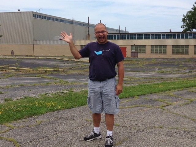 Waving goofball standing in the empty parking lot of a factory.