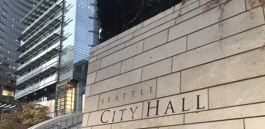 Downtown Seattle wall with City Hall sign on it and buildings in the background.