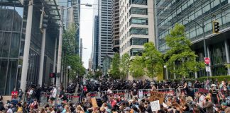 The view of Fifth Avenue with a cordon of police officers brandishing billy clubs protecting the block in front of city hall and a stream of protests headed down James Street.