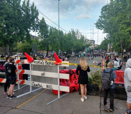 SPD Hopes to Reclaim East Precinct from CHAZ, but Protesters Say Finders Keepers People look on a cordoned off Pine Street just before protesters add "Black Lives Matter Way" in big block letters. (Photo by author)