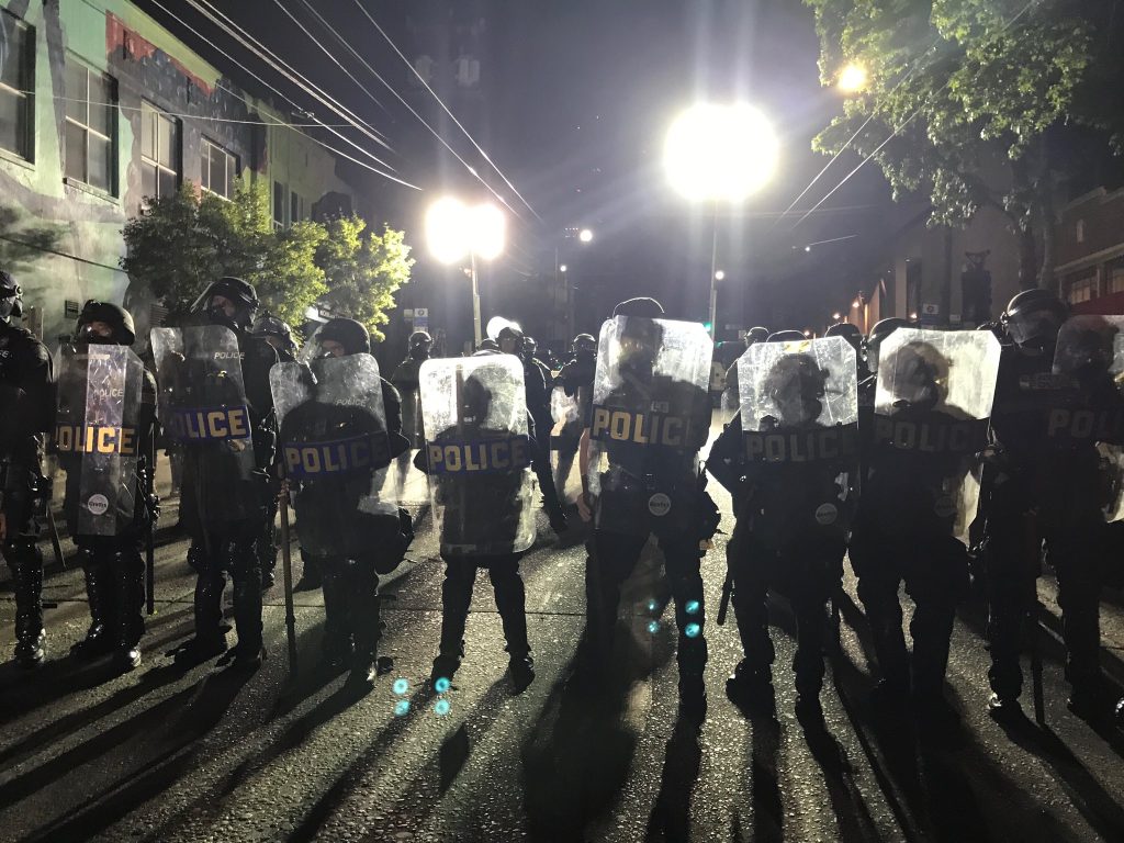 A wall of police with riot shields outside East Precinct.