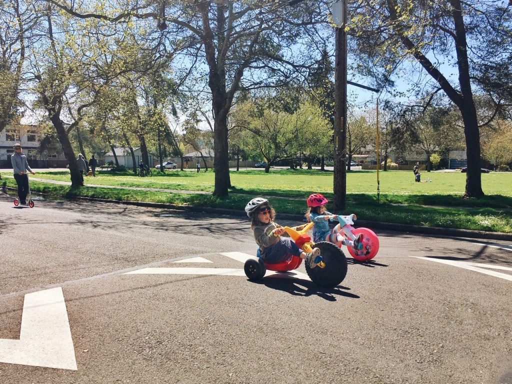 Two young kids on trikes in an open street.