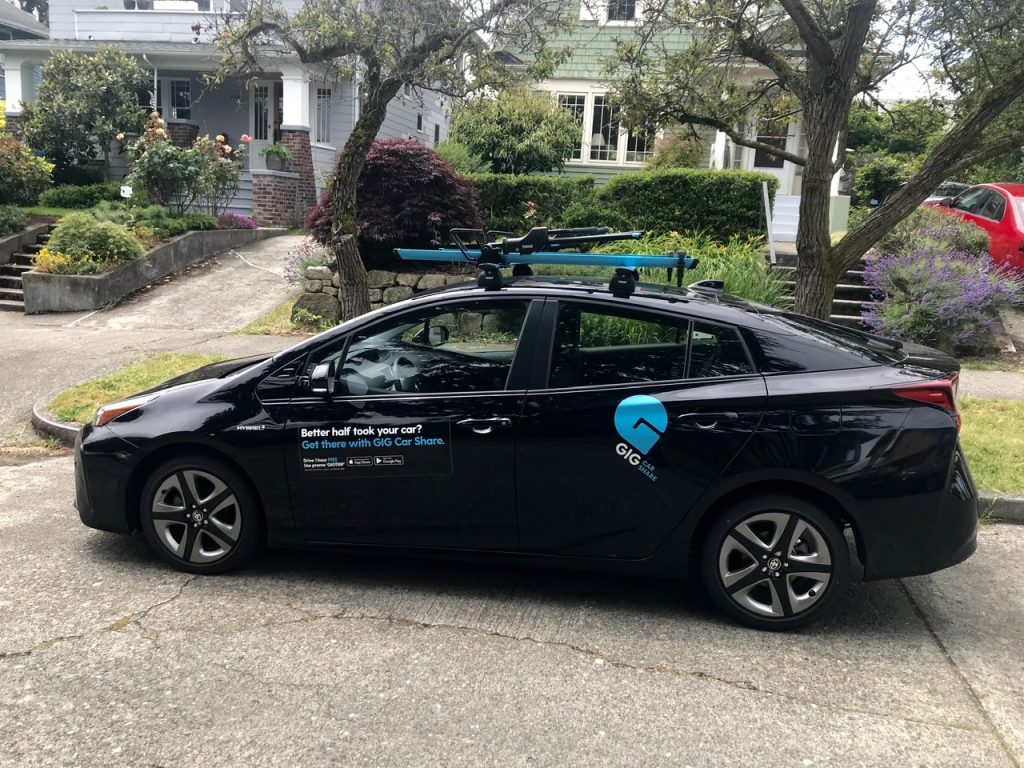 Black sedan with GIG car share branding in front of a single family house