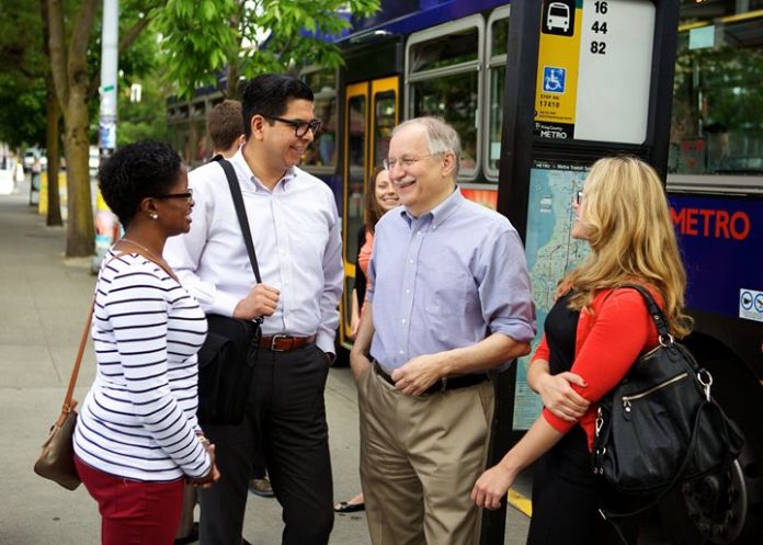 Frank Chopp smiles next to three transit riders at a bus stop.