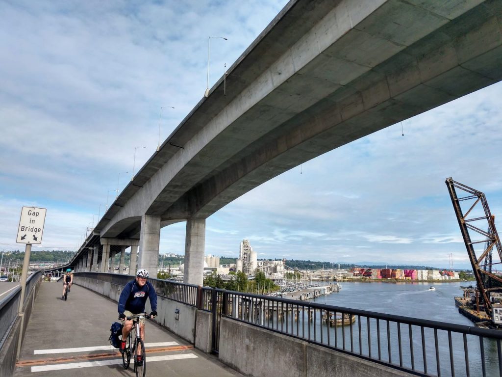 People bike on the low bridge with the cracked high bridge looming overhead. (Photo by Doug Trumm)