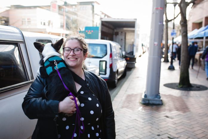 Jessi Murray poses on the sidewalk with her dog in her arms.