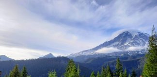 Clouds crown Mount Rainier as a few cars stop for passengers to take in the view.