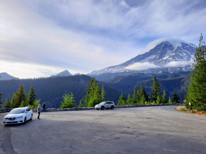 Clouds crown Mount Rainier as a few cars stop for passengers to take in the view.