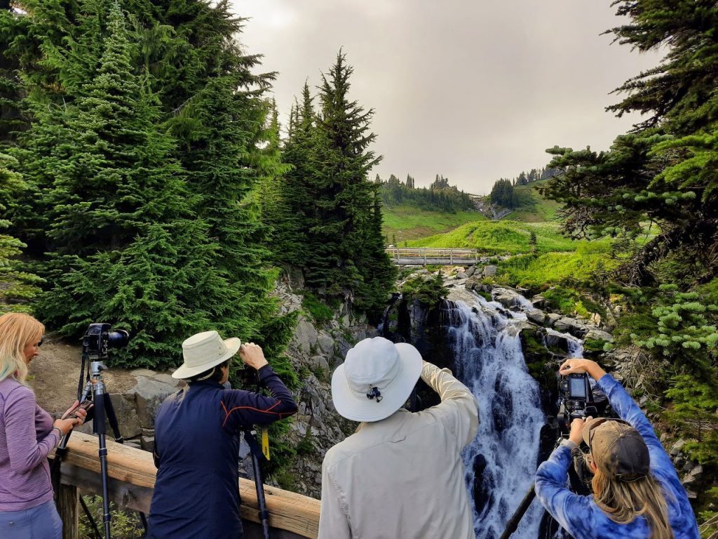 Four photographers with tripods point their camera at Myrtle Falls from a viewing ledge near Paradise. 