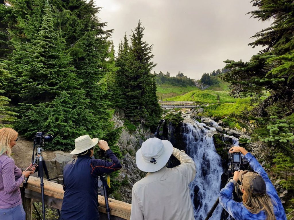 Four photographers with tripods point their camera at Myrtle Falls from a viewing ledge near Paradise.