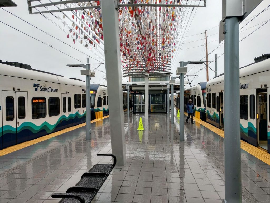 two trains at a station with little glass orbs sculpture overhead