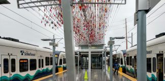 two trains at a station with little glass orbs sculpture overhead