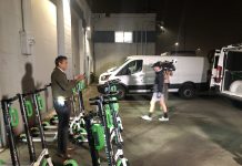 Lime Rolls Out Scootershare in Seattle, LINK and Wheels a Month Away A reporter stands amidst scooters in a garage for a TV spot.